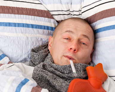 Kranker Mann mit Wärmeflasche und Fieberthermometer